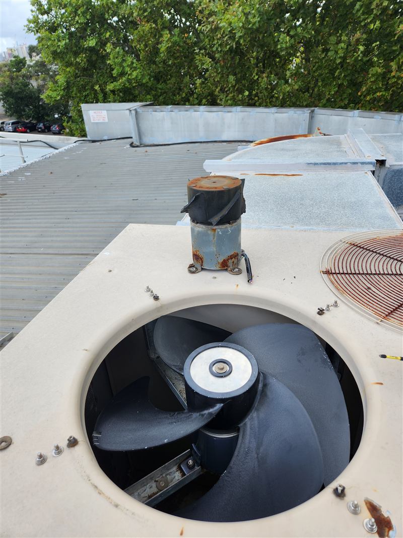 A rooftop condenser with its fan motor removed, on a commercial roof